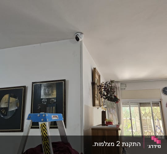 מצלמת אבטחה מותקנת בפינת תקרה בחדר עם סולם ותמונות